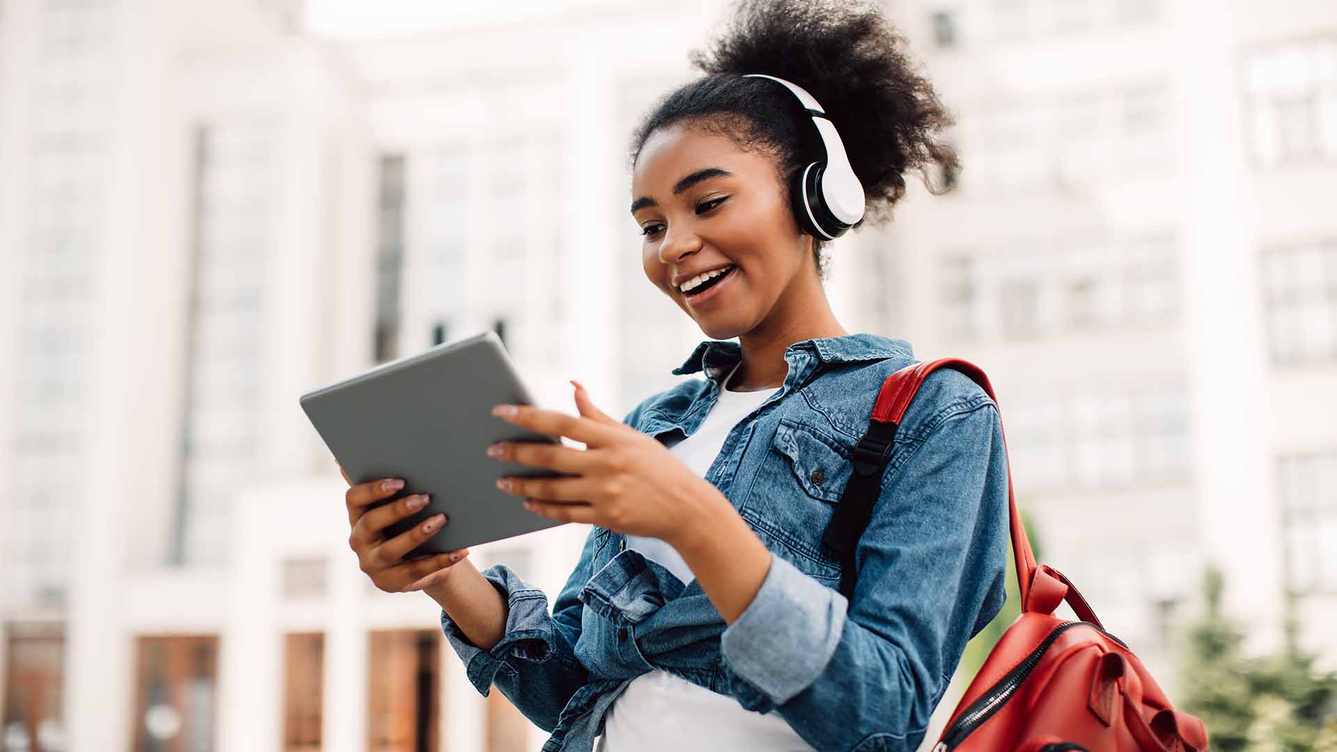 Imagem de uma jovem com sorriso no rosto, fone de ouvido e tablet nas mãos, caracterizando o artigo: "Profissões do futuro: você sabe quais são?"