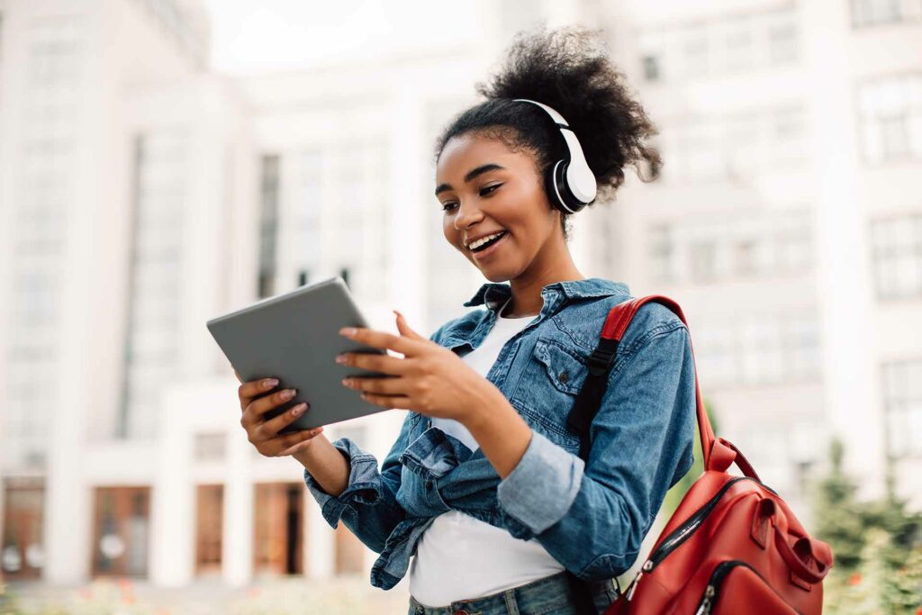 Imagem de uma jovem com sorriso no rosto, fone de ouvido e tablet nas mãos, caracterizando o artigo: "Profissões do futuro: você sabe quais são?"